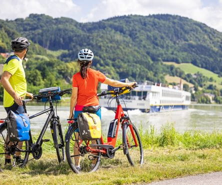 Cyclists on the Danube cycle path look at a passing ship 