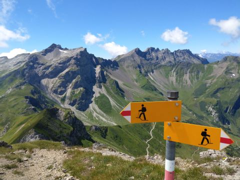 A hiking signpost stands in front of a green mountain backdrop in Liechtenstein.